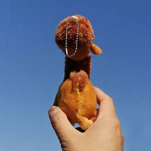 Back view of a cute plush camel keychain charm held against a clear blue sky