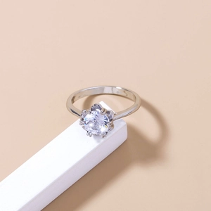 Detailed view of silver ring with six-prong set round clear gemstone on beige background