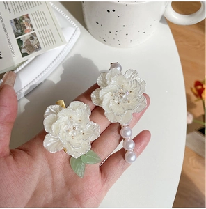 Dettaglio di fermagli per capelli con camelia bianca, foglie in resina e perle finte
