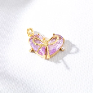 Gold heart pendant with pink zircon and bow detail on textured white fabric