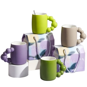 Minimalist ceramic mugs with bubble handles in purple, green, and beige with gift bags