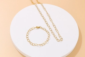 Detail view of gold metal link chain necklace and bracelet on a white display stand