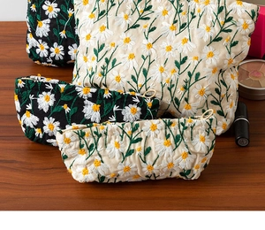 Close-up of daisy embroidery detail on canvas makeup bags with gold ring zippers
