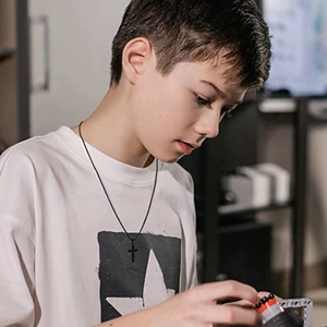 Close-up of a young boy wearing a minimalist black titanium cross pendant on a rope chain