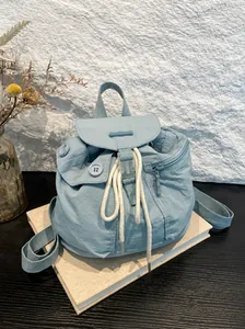Light blue nylon drawstring backpack with button detail on minimalist beige books