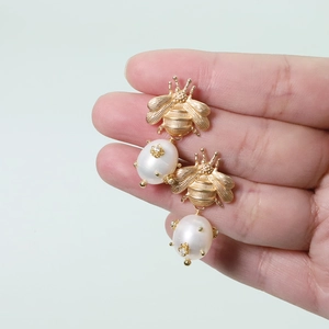 Detail of gold bee earrings featuring freshwater pearls held in hand for scale