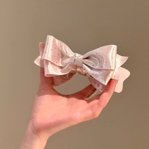 Close-up of pink polka dot bow hair clip with satin texture and black spots