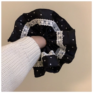 Detail of black polka dot scrunchie with white lace trim worn on a woman's wrist
