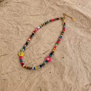 Close-up of colorful seed bead necklace with yellow smiley and pink flower pendant