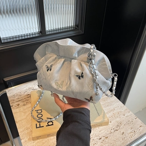 Silver pleated bucket bag with metallic butterflies and woven chain strap held in hand