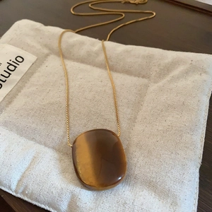 Detailed view of an oval tiger eye stone pendant on a delicate gold box chain necklace