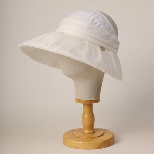Detail of white wide-brim sun hat featuring elegant ruffled edges and a gold metal accent
