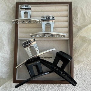 Minimalist metal shark hair clips in silver and black finishes displayed in a wooden box
