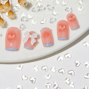 Pink French tips nail press-ons with 3D hearts, white bows and pearls on a white plate
