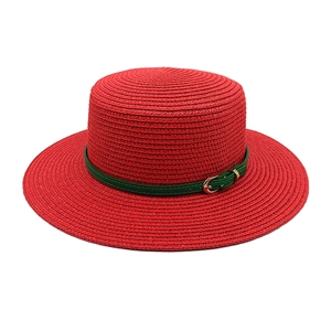 Vue détaillée du chapeau de paille rouge avec bande en cuir vert et boucle métallique dorée