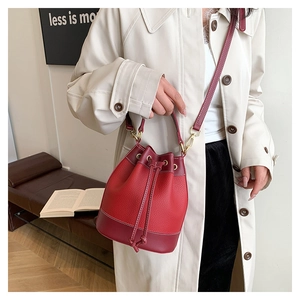 Sac seau rouge en cuir grainé avec cordon de serrage porté sur un trench-coat beige