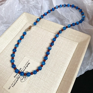 Detailed shot of blue agate beaded necklace with red spacers on textured background