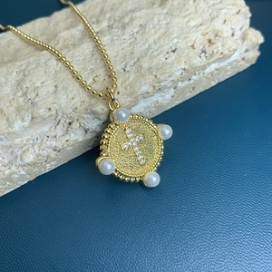 Golden round cross pendant with white pearls and rhinestones on blue stone background