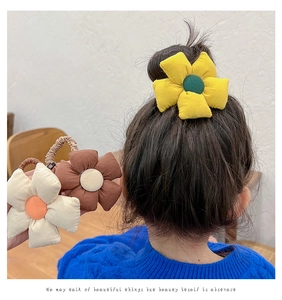 Detailed view of three cloth flower hair ties in yellow, brown, and cream colors