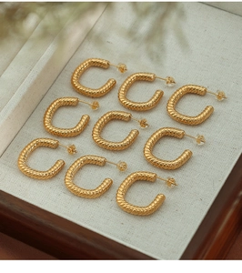 Detailed view of nine gold twisted rope C-shaped stud earrings on a beige velvet tray
