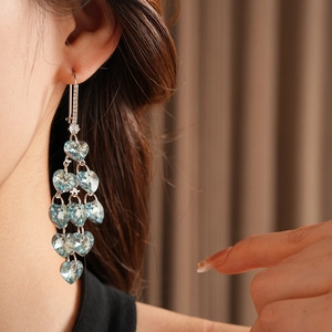 Detail of light blue heart-shaped crystal tassel earrings worn on female model's ear