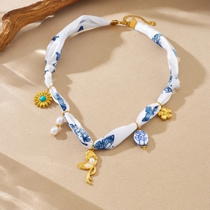 Detail of silk ribbon necklace with blue butterfly print and golden charms on sand background
