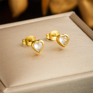 Macro shot of gold heart-shaped stud earrings with clear crystals on beige jewelry box