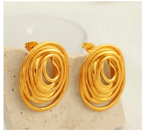Close-up of golden spiral stud earrings on a textured stone base showing metallic luster