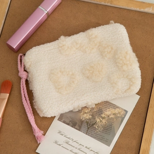 Detail of plush cream lamb wool makeup bag featuring a pink woven tassel zipper pull