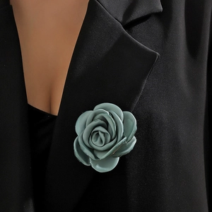 Close-up of green fabric rose brooch on black suit lapel showing satin texture