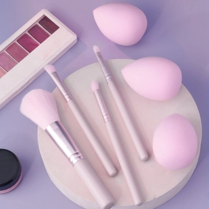 Macro view of pink makeup brush set with blending sponges and eyeshadow palette on stone base