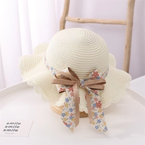 Close-up of children's straw hat with floral ribbon, bow detail, and wavy lace edge