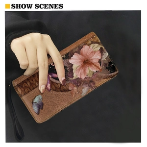 Detail of brown leather wallet featuring floral prints and wrist strap in model's hand
