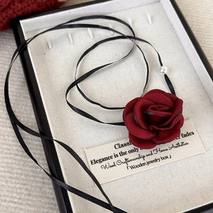Macro detail of wine red fabric rose necklace with black satin ribbon and pearl detail