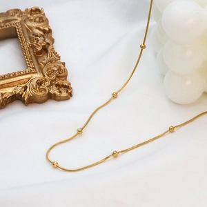 Close-up of 18k gold plated snake chain necklace with small beads on white fabric