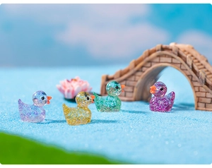 Close-up of glitter resin duck figurines in purple and yellow on a blue sand landscape