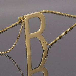 Vue macro d'un collier avec pendentif lettre R plaqué or 18K et reflet sur fond noir