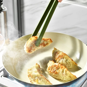 Green heat-resistant silicone kitchen tongs picking up a fried dumpling for cooking