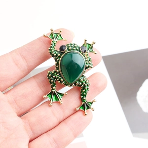 Macro detail of frog-shaped brooch with green teardrop gemstone and gold-tone base