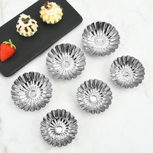 Flat lay of flower-shaped metal baking molds and tart cups on white marble surface