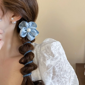 Détail d'un élastique en satin bleu avec perle porté sur une coiffure tressée
