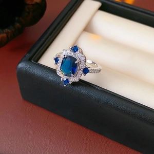 Vue macro d'une bague avec pierre bleue rectangulaire et halo de diamants en boîte