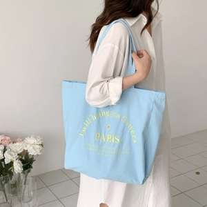 Detail of light blue canvas tote bag with yellow floral embroidery and letter print