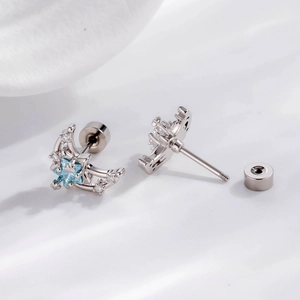 Silver celestial moon and blue star stud earrings on soft white silk fabric background