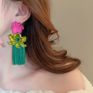 Détail de boucles d'oreilles fleurs avec pétales magenta et longues franges de pompons