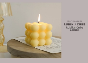 Close-up of a lit cream bubble cube candle on a wooden stand with warm lighting