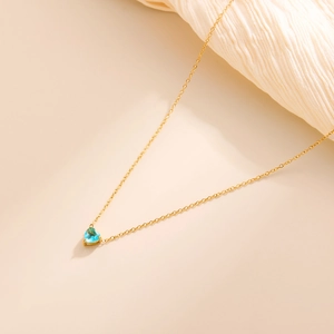 Macro detail of heart-shaped light blue gemstone necklace with 18k gold plated chain