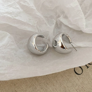 Detailed view of silver C-shaped metallic hoop earrings on textured fabric and paper