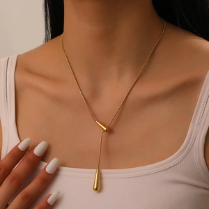 Detail of golden double water drop pendants on sleek snake chain worn by a model