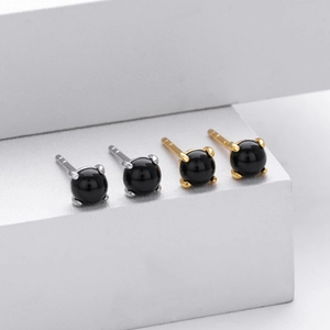 Macro detail of minimalist black stone stud earrings in gold and silver four-prong settings